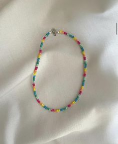 a colorful beaded bracelet is laying on a white sheet and has a silver charm