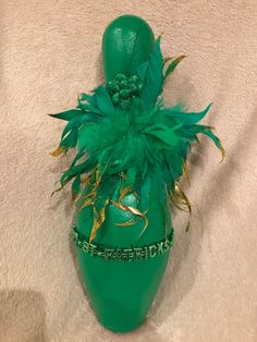 a green vase with feathers on it sitting on a white cloth covered floor next to a wall