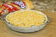 an uncooked casserole with cheese on top and two bags of chips in the background