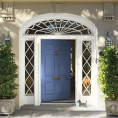 a blue front door with an arched window and potted plants on the side walk