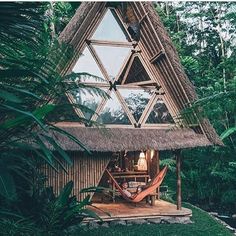 a house made out of wood and grass with a hammock hanging from the roof