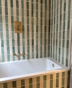 a bath tub sitting next to a wall with green and white tiles on it's sides