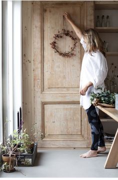 a woman standing in front of a wooden door pointing at a wreath on the wall