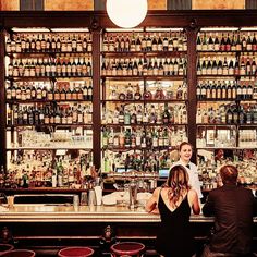 two people sitting at a bar with lots of bottles behind them