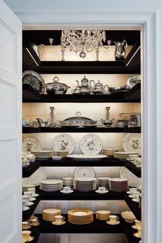 an open pantry filled with lots of plates and bowls on top of black shelving