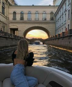 a woman sitting on the back of a boat in front of a bridge at sunset