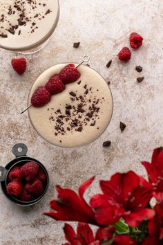 two desserts with raspberries and chocolate shaving on them next to red flowers