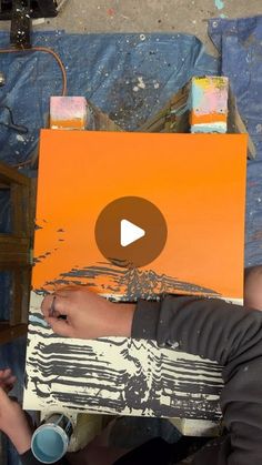 a person holding up an orange piece of art that has been painted with acrylic paint