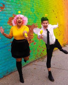 two people dressed in costumes are posing for a photo near a brick wall with graffiti on it