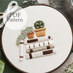 the embroidery pattern shows a potted cactus and other plants on top of a table