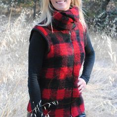 a woman wearing a red and black plaid vest standing in tall grass with her hands on her hips