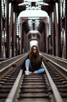 a woman sitting on train tracks in the middle of an old bridge with her legs crossed