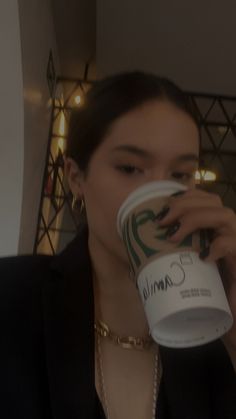 a woman drinking from a coffee cup with a chain around her neck and wearing a black blazer