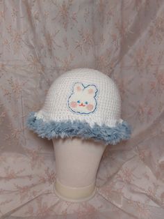 a crocheted hat with a bear on the front and blue fur around the brim