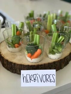 small cups filled with vegetables sitting on top of a wooden tray next to a sign