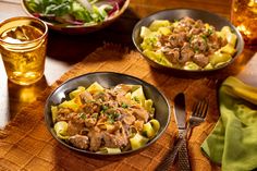 two bowls filled with pasta and meat on top of a wooden table next to drinks