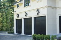 two black garage doors are on the side of a white building with trees in the background