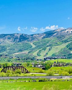 an old train bridge in the middle of a green valley with mountains in the background