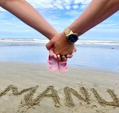 two people holding hands while standing in front of the ocean with sand written on it