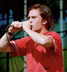 a man with long hair holding a microphone to his mouth as he sings into the mic