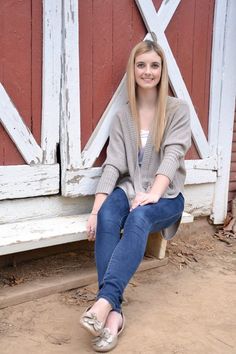 a woman sitting on a bench in front of a barn door with her legs crossed