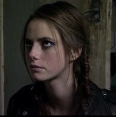 a woman with braids in her hair looks into the distance while wearing a leather jacket