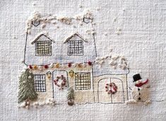 two embroidered houses with snowmen and wreaths on the outside, one in front of the other