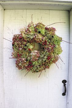 a wreath hanging on the side of a white door with red and green flowers in it