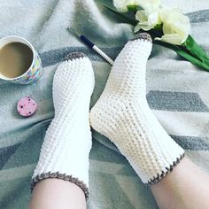 a pair of white knitted mittens sitting on top of a bed next to a cup of coffee