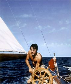 a man on a sailboat in the ocean next to a boat with a steering wheel