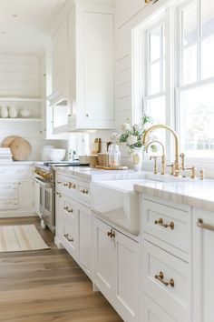 a kitchen with white cabinets and wood flooring is pictured in this image, the sink has gold faucets on it