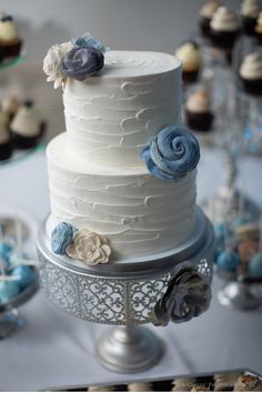 a wedding cake with blue and white flowers on the top is surrounded by cupcakes