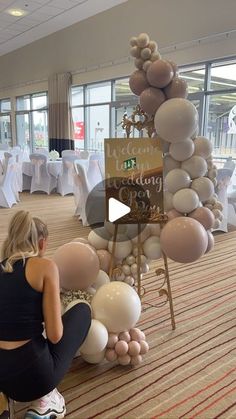 a woman sitting on a stool in front of a table with white and pink balloons