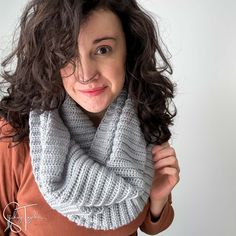 a woman with curly hair wearing a gray knitted cowl scarf and brown sweater