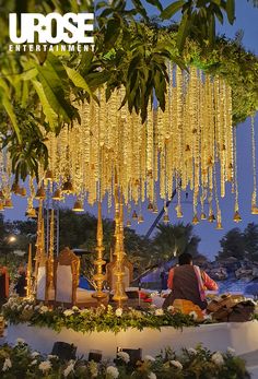 a man sitting under a tree filled with lots of gold colored beads hanging from it's branches