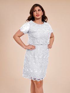 a woman wearing a white dress with short sleeves and lace on the shoulders, standing in front of a beige background