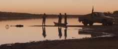 three people standing on the beach next to a truck with a boat in the water