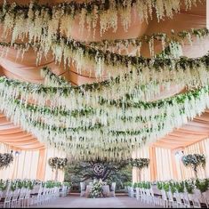 an indoor wedding venue with white chairs and flowers hanging from the ceiling