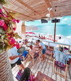 people are sitting at tables on the deck overlooking the ocean and beach with umbrellas