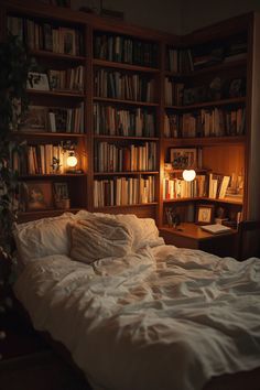 an unmade bed sitting in front of a book shelf filled with books and lights