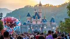 a crowd of people standing in front of a castle with balloons on it's head