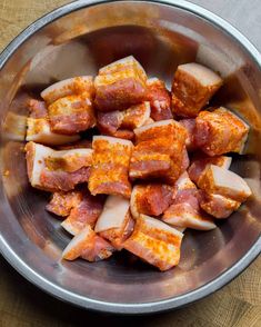 a metal bowl filled with sliced meat on top of a wooden table