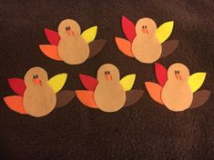 four felt turkeys with leaves on them sitting on a black surface in front of a brown towel