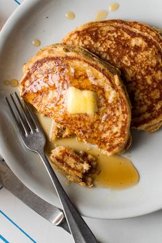 two pancakes with butter and syrup on a white plate next to a knife and fork