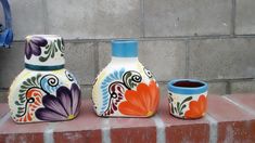 three colorful vases sitting on top of a brick wall