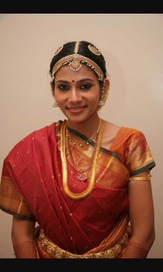 a woman in a red and gold sari with jewelry on her neck, smiling at the camera