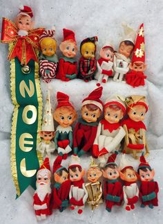 a group of elf figurines sitting next to a green ribbon on top of snow covered ground