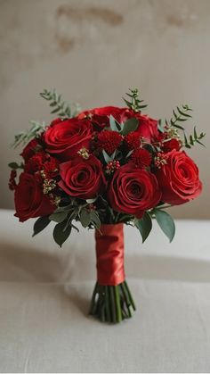 a bouquet of red roses and greenery in a vase