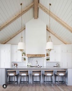 a large kitchen with white cabinets and wooden beams on the ceiling, along with bar stools