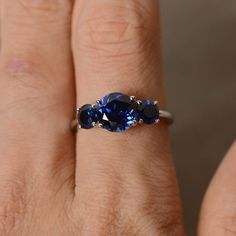 a woman's hand with three blue sapphires on her finger and an engagement ring